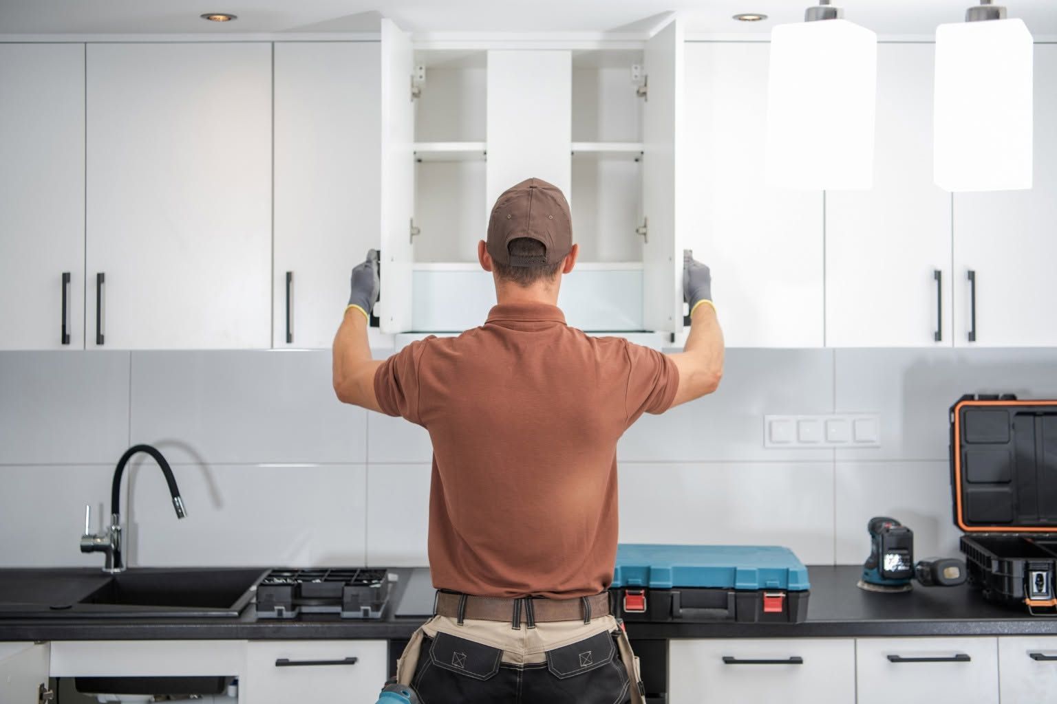 Person installing white kitchen cabinets with arms raised in a bright modern kitchen.