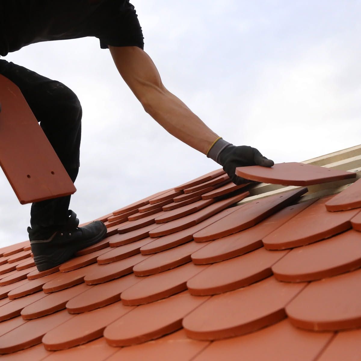 Worker laying red roof tiles with a trowel on a sloped roof