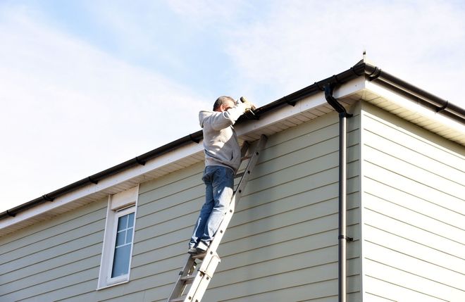 Person on a ladder repairing roof trim on a beige house