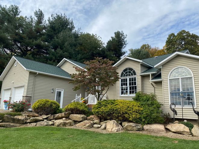 Suburban house with beige siding, stone accents, and landscaped front yard under a cloudy sky
