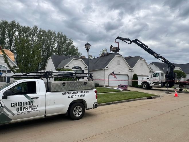 Utility truck and crane working on a damaged white house in a suburban street after a storm