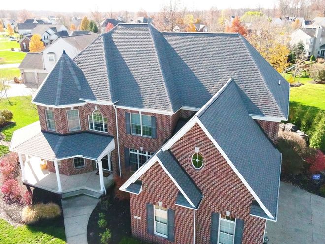 Aerial view of a large brick house with a gray roof and white porch in a suburban neighborhood.