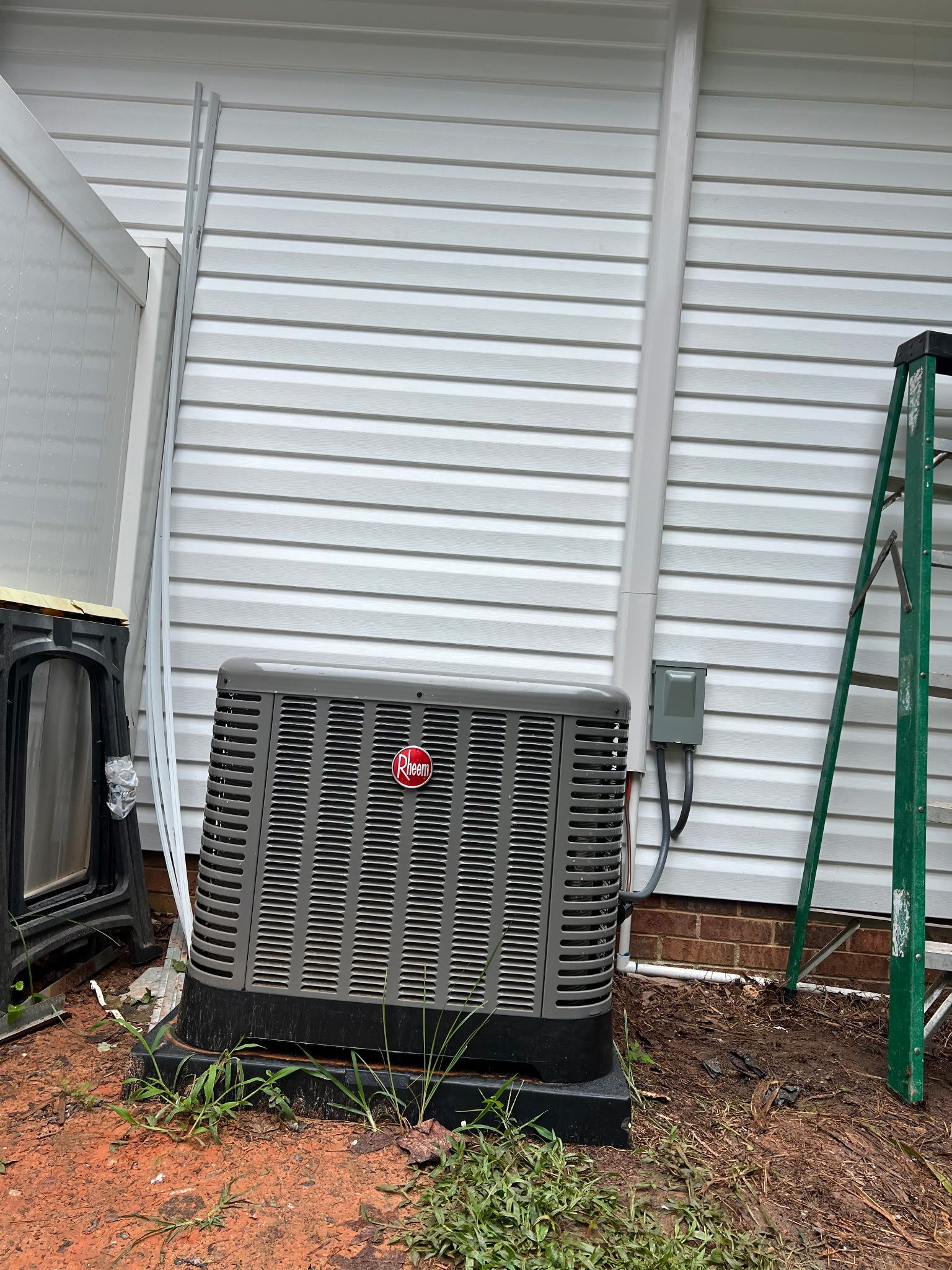 Outdoor HVAC unit beside a white house wall with a green ladder leaning nearby.