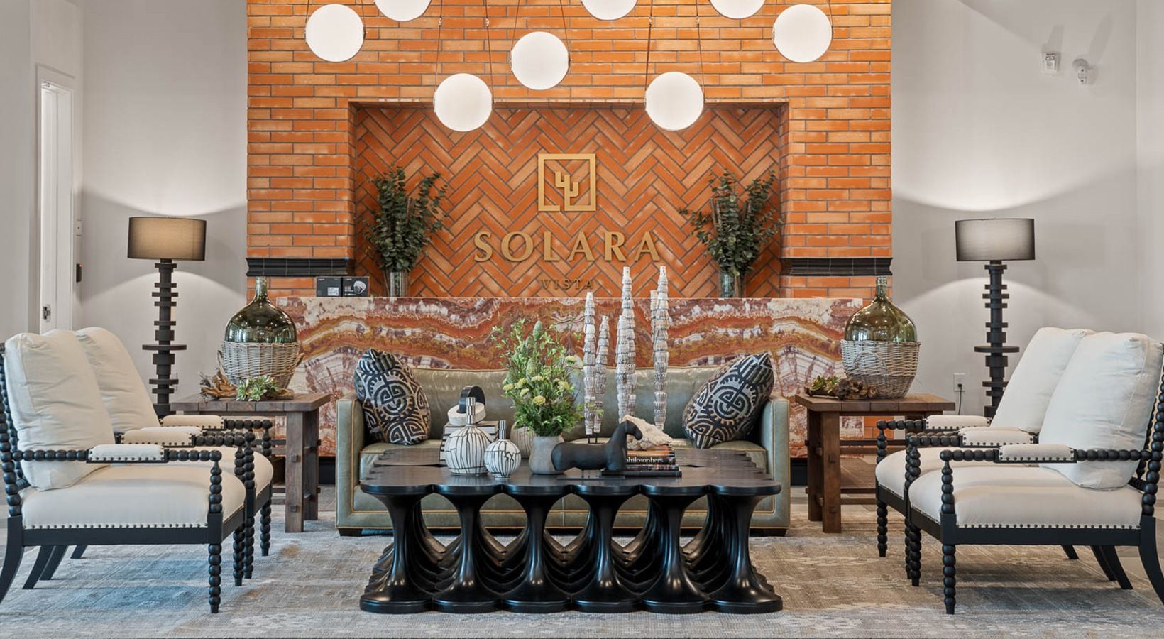 Elegant room with brick fireplace, symmetrical white chairs, black coffee table, and decorative plants.