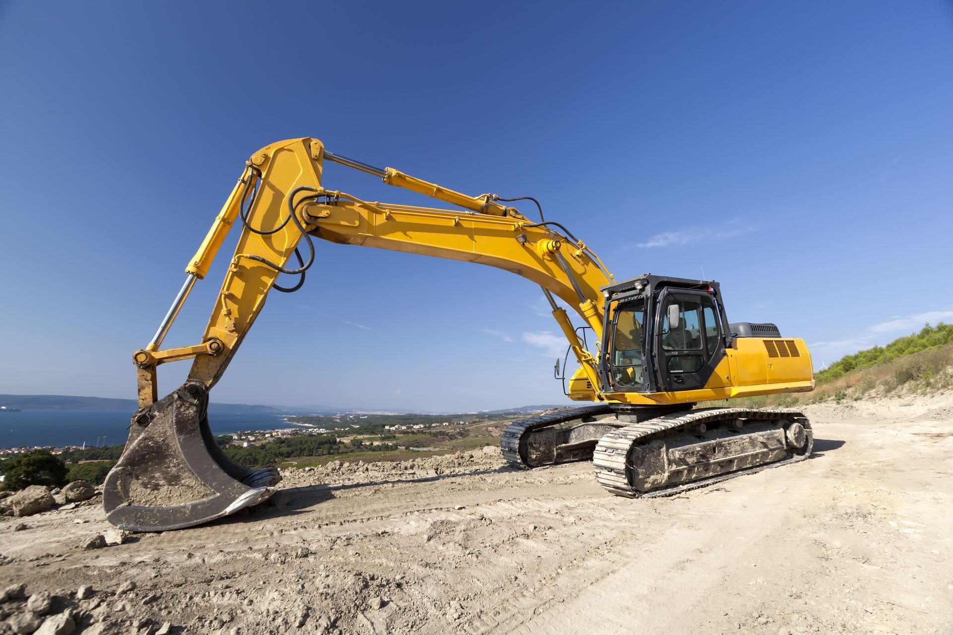 Yellow excavator on a dirt construction site under a clear blue sky
