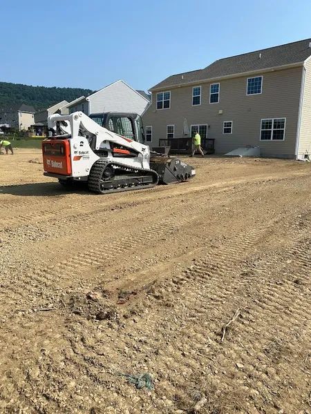Skid steer leveling dirt beside a beige house under construction on a sunny day
