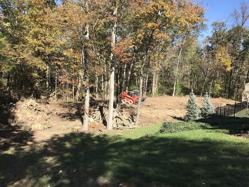Autumn wooded hillside with a red tractor beside a rock pile near a grassy yard
