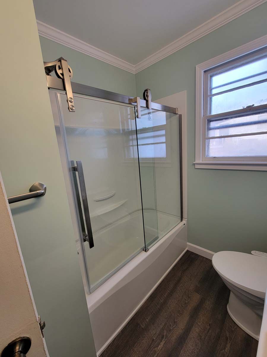 A bathroom with a toilet , tub , shower and window.