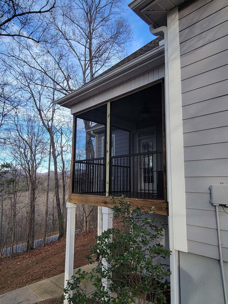 A screened in porch on the side of a house with trees in the background.
