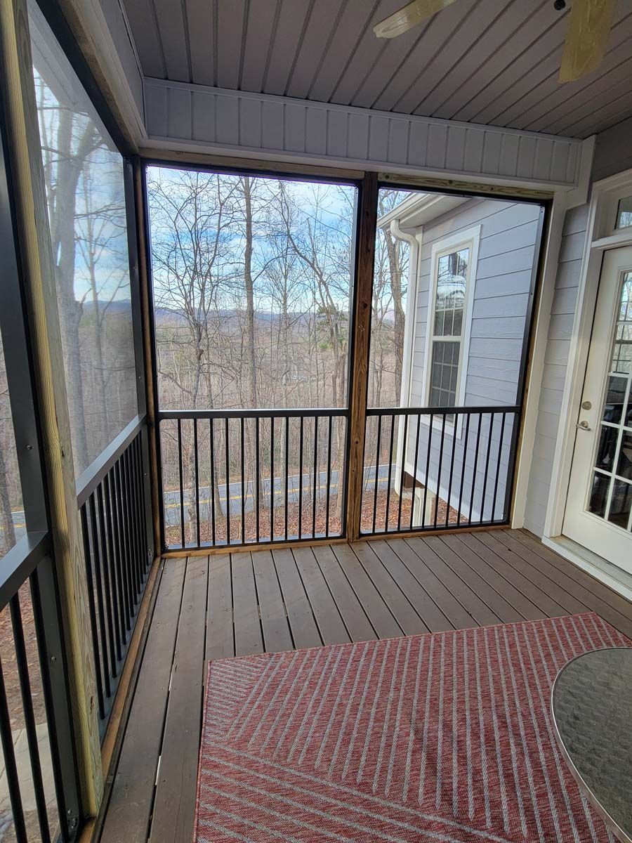 A screened in porch with a ceiling fan and a view of the woods.