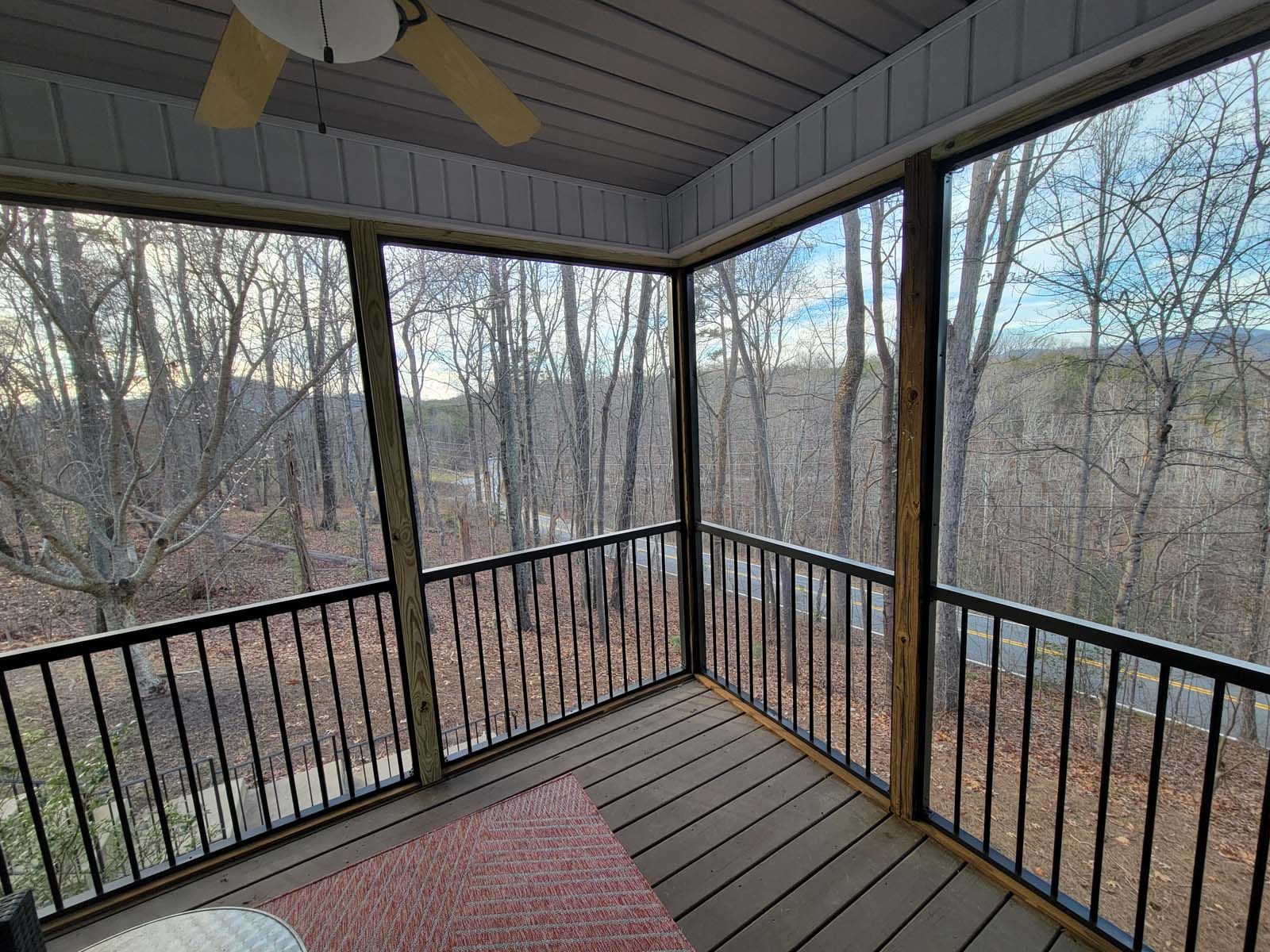 A screened in porch with a ceiling fan and a view of the woods.