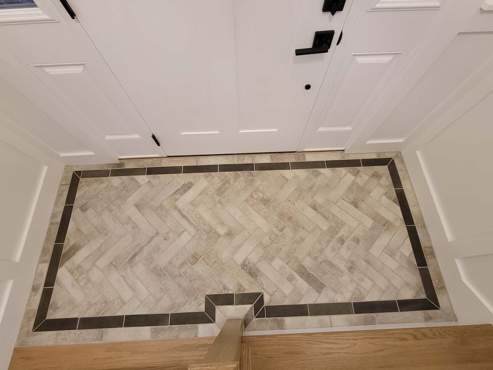 A herringbone tile floor in a hallway next to a door.