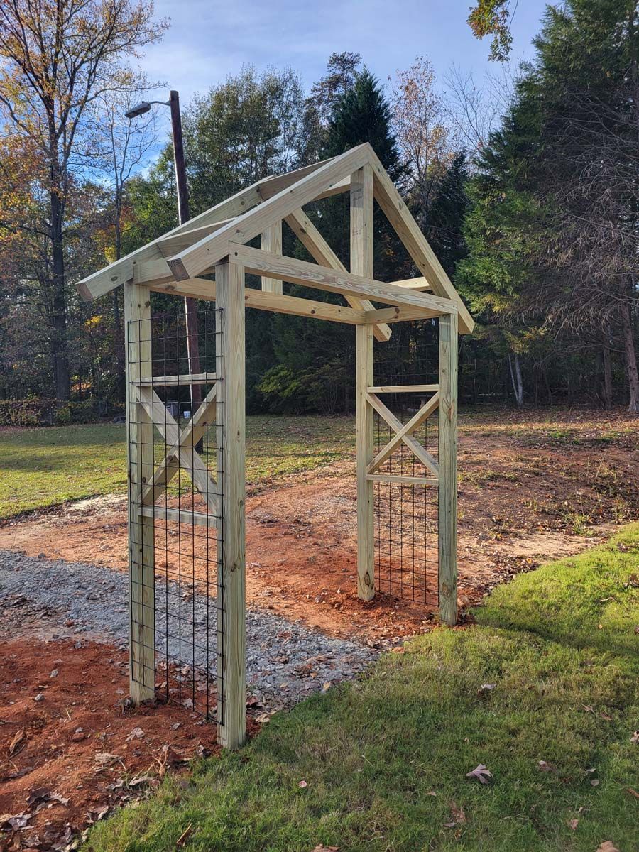 A wooden archway is being built in a yard with trees in the background.