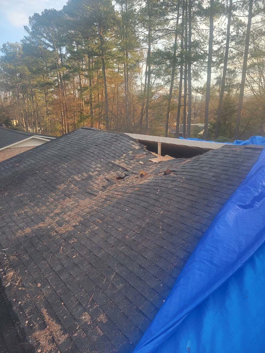 A roof with a hole in it is covered in a blue tarp.