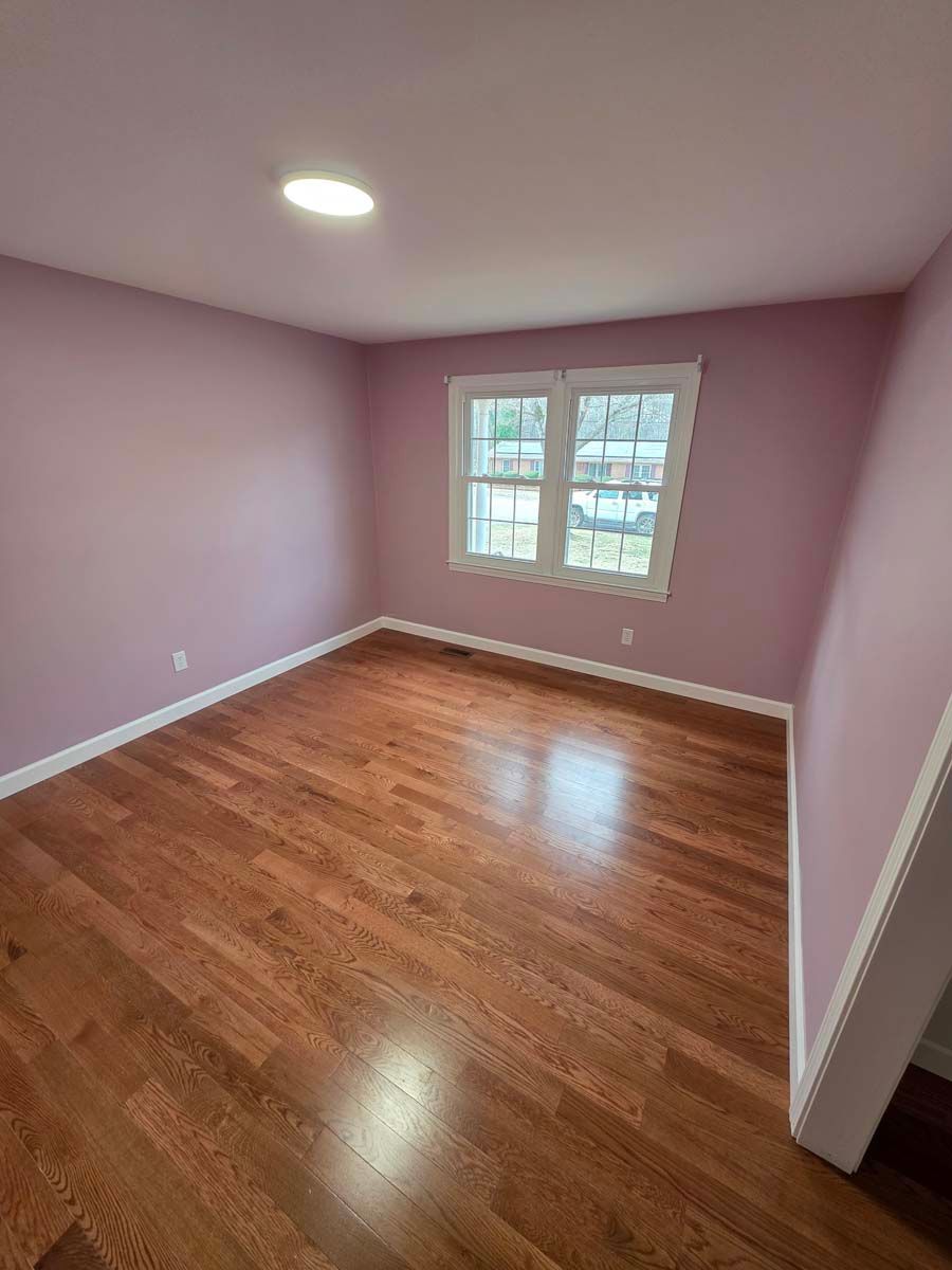 An empty room with pink walls and hardwood floors.