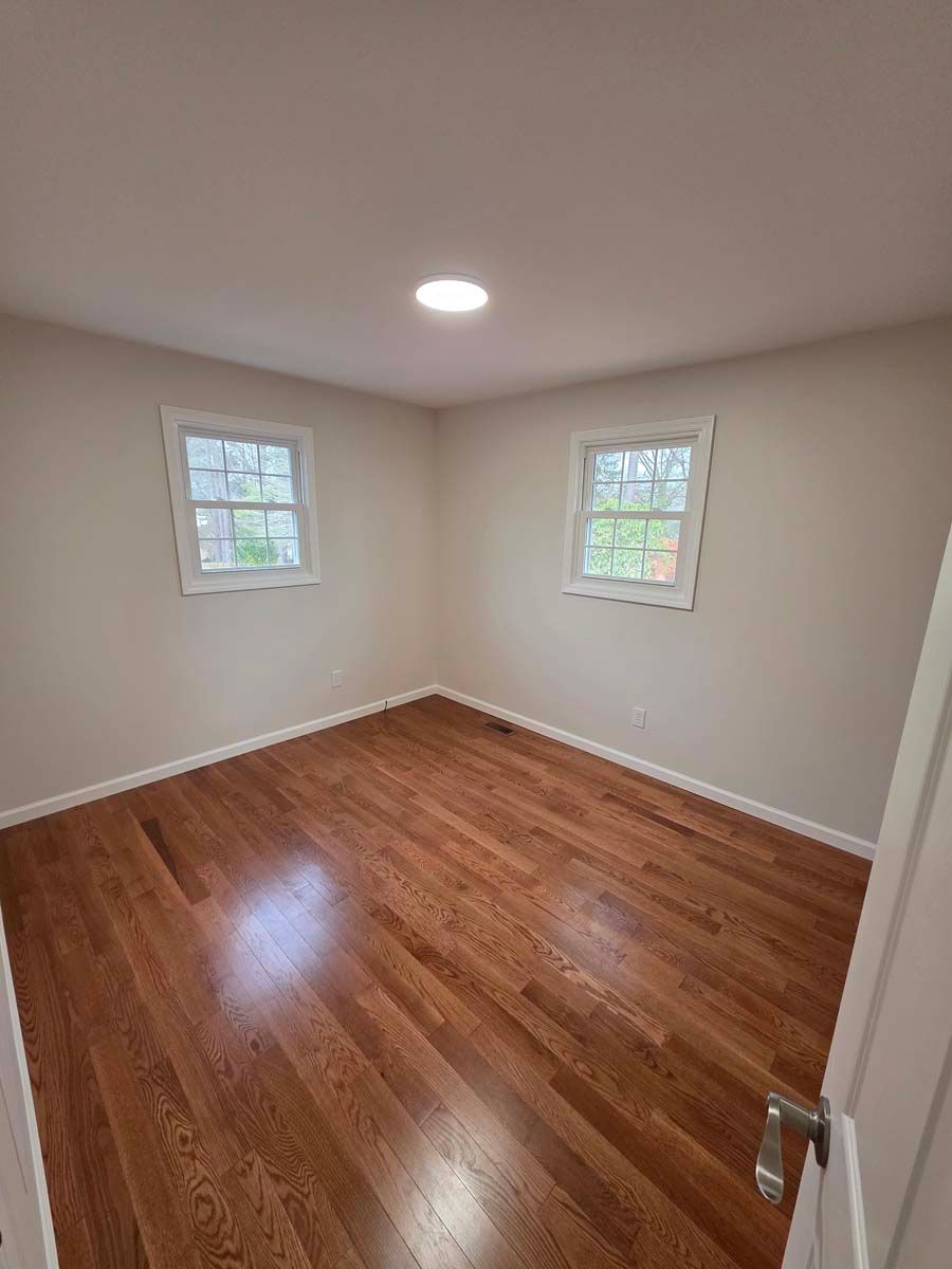 An empty bedroom with hardwood floors and two windows.