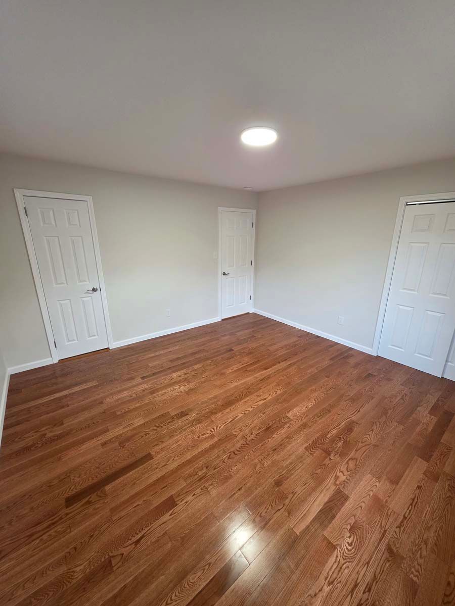 An empty bedroom with hardwood floors and white walls.