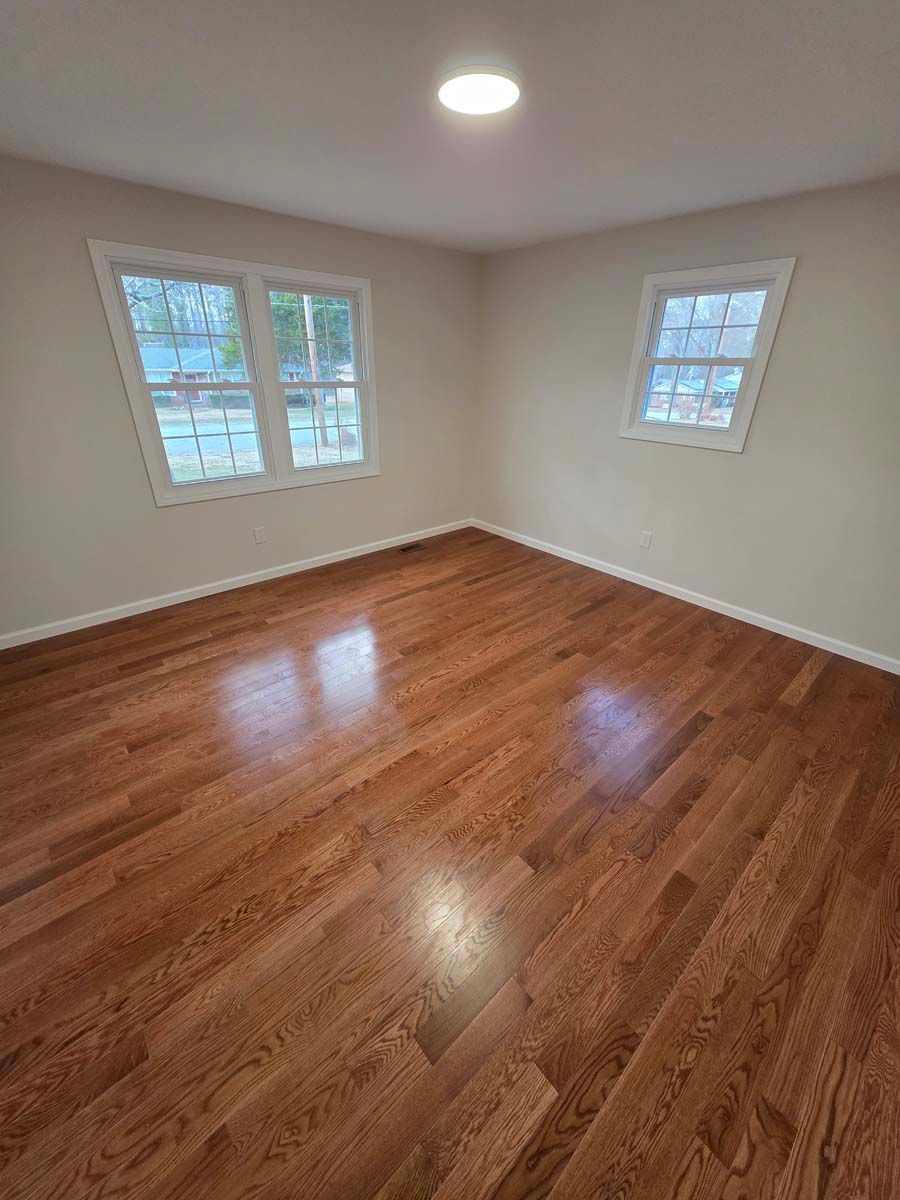 An empty room with hardwood floors and two windows.