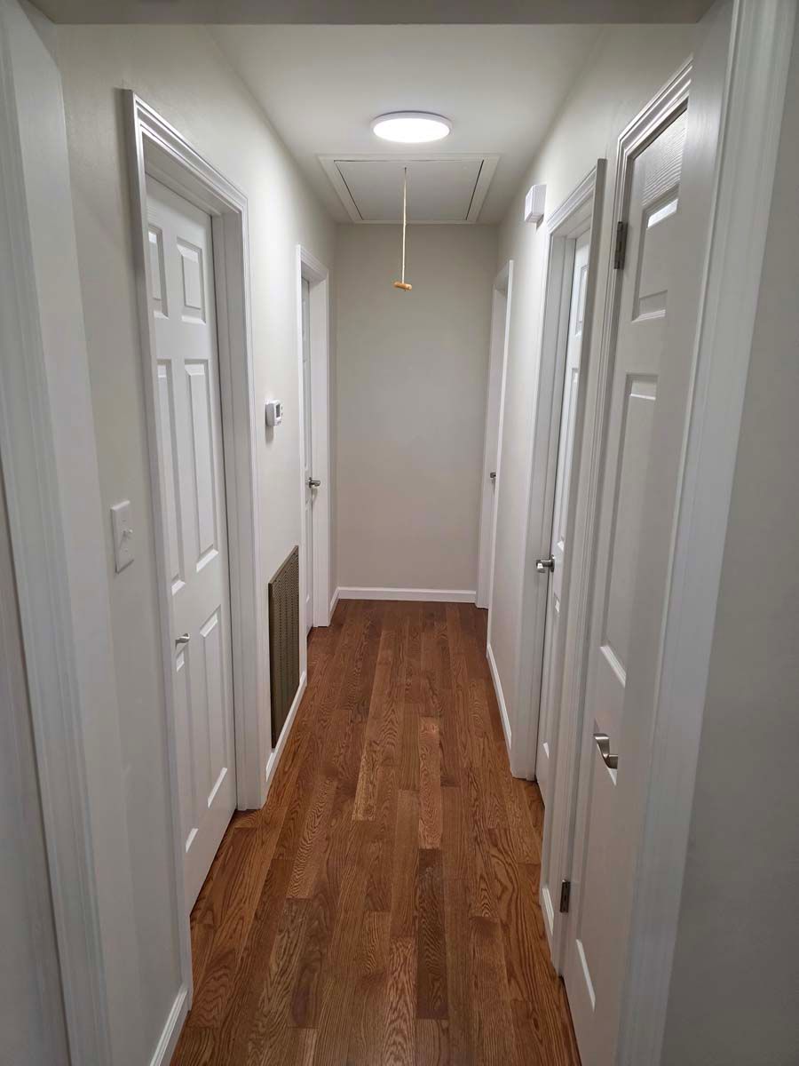 A long hallway with hardwood floors and white doors in a house.
