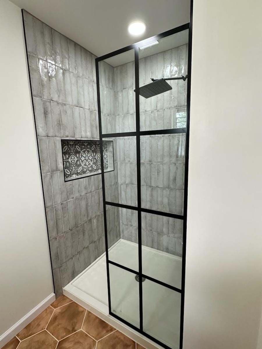 A bathroom with a walk in shower with a black frame and a shower head.