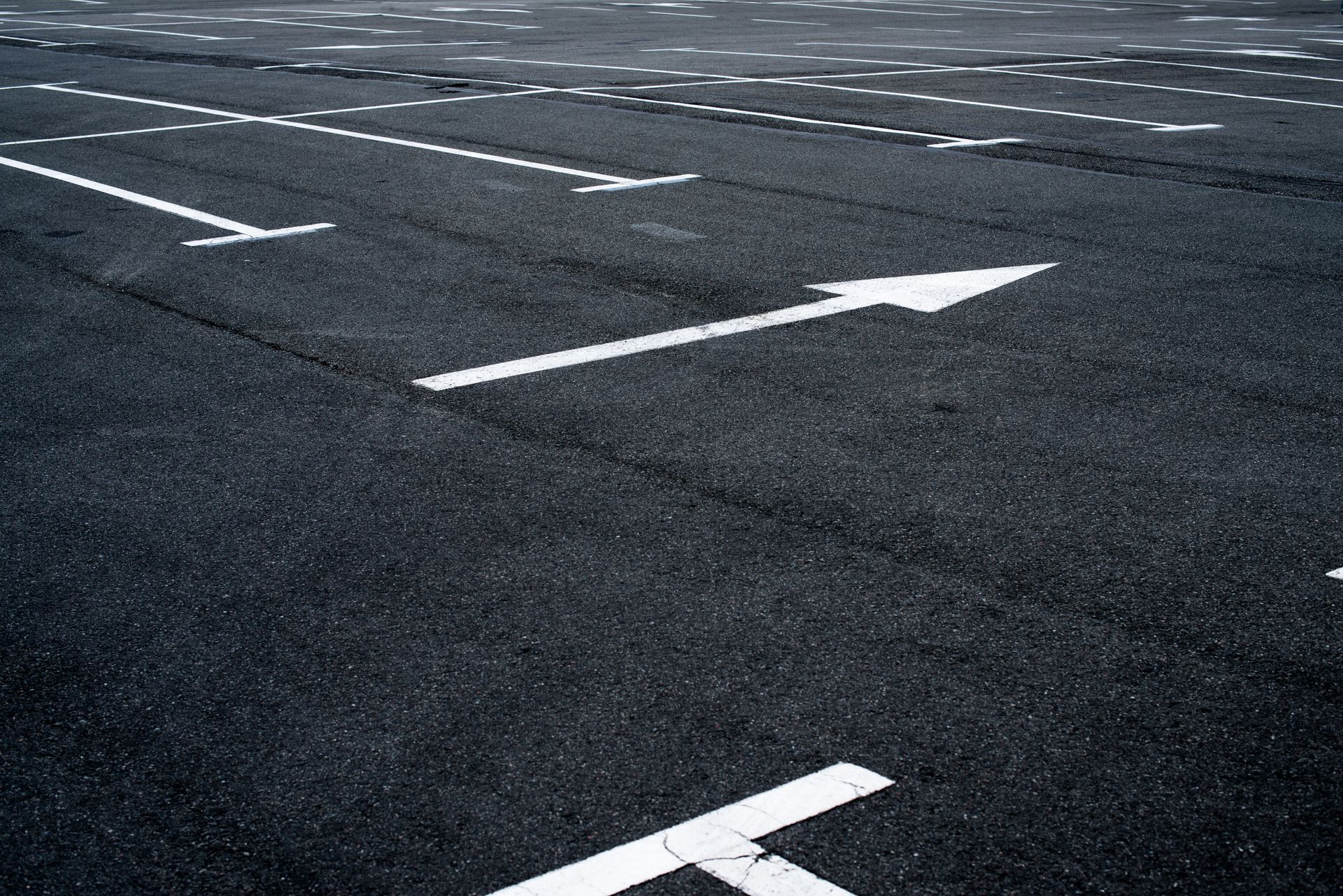 An asphalt parking lot with white painted parking space lines and a directional arrow.
