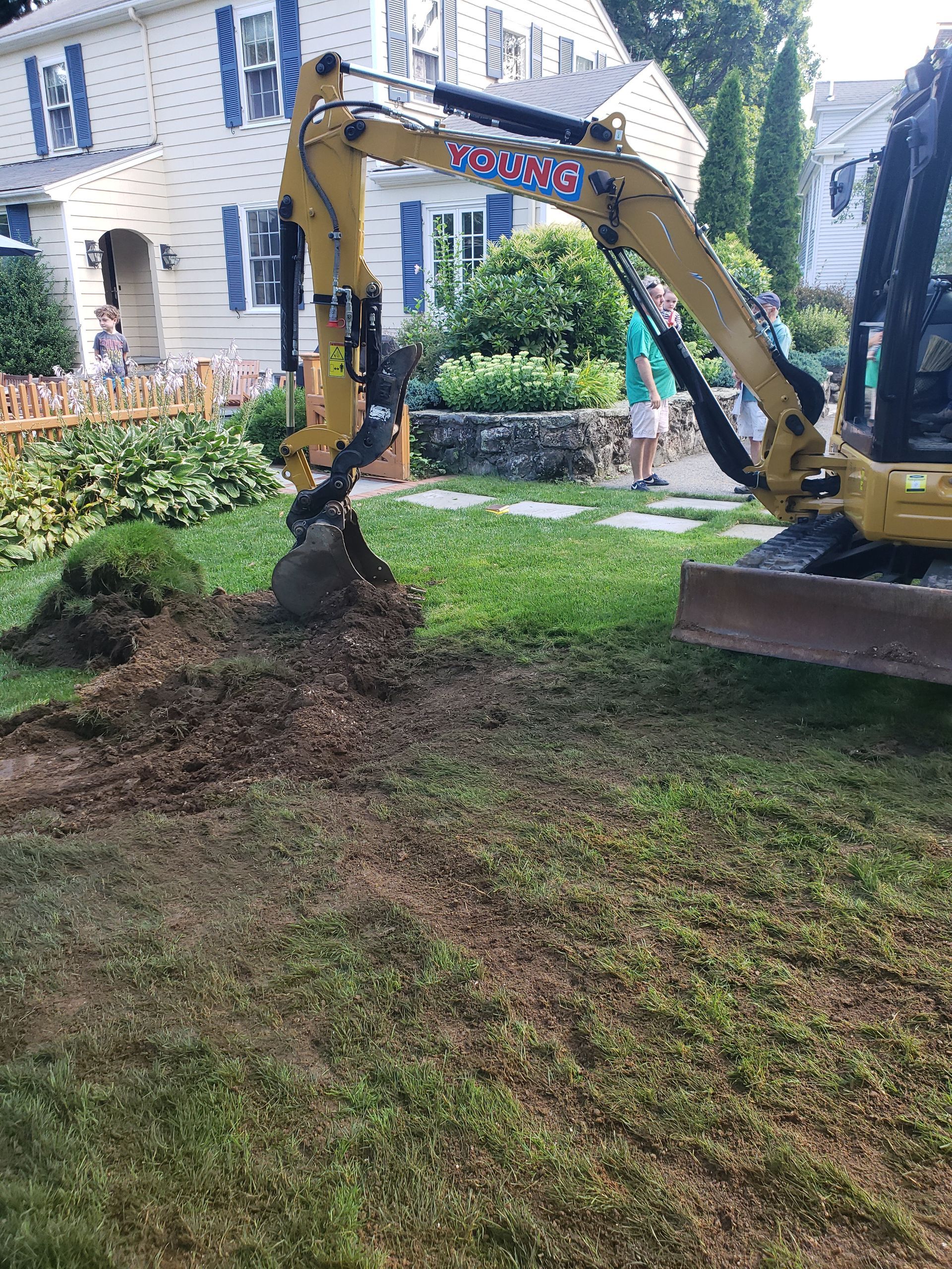 a yellow excavator is digging a hole in the grass in front of a house