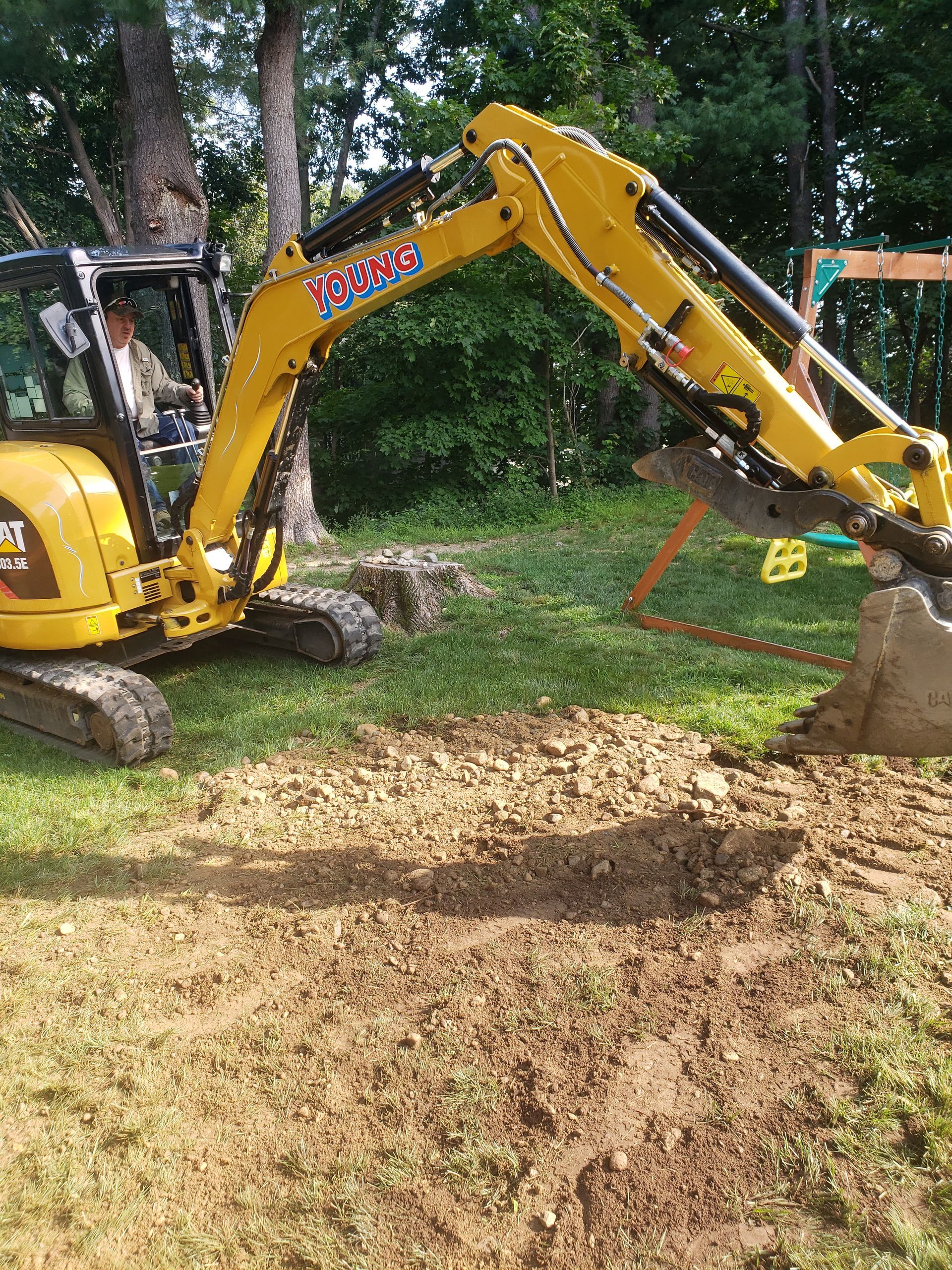 a yellow excavator is digging a hole in the dirt in a yard