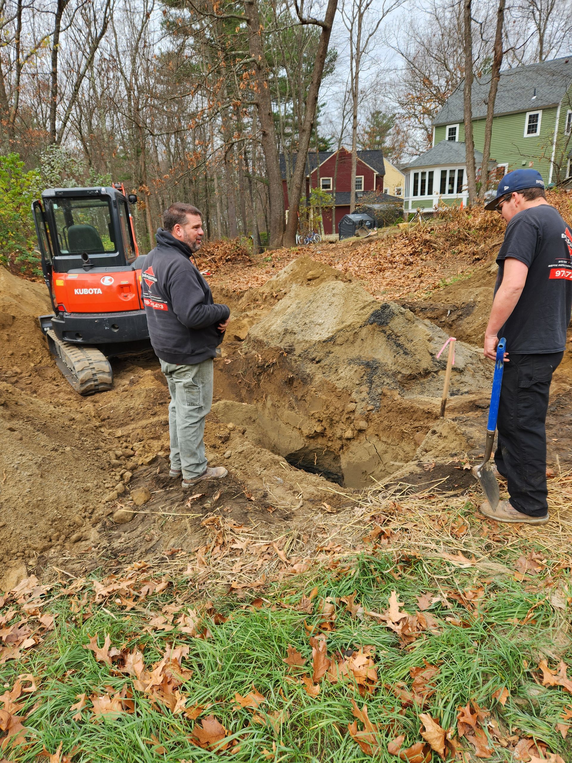 two men are standing in front of an excavator in a dirt field