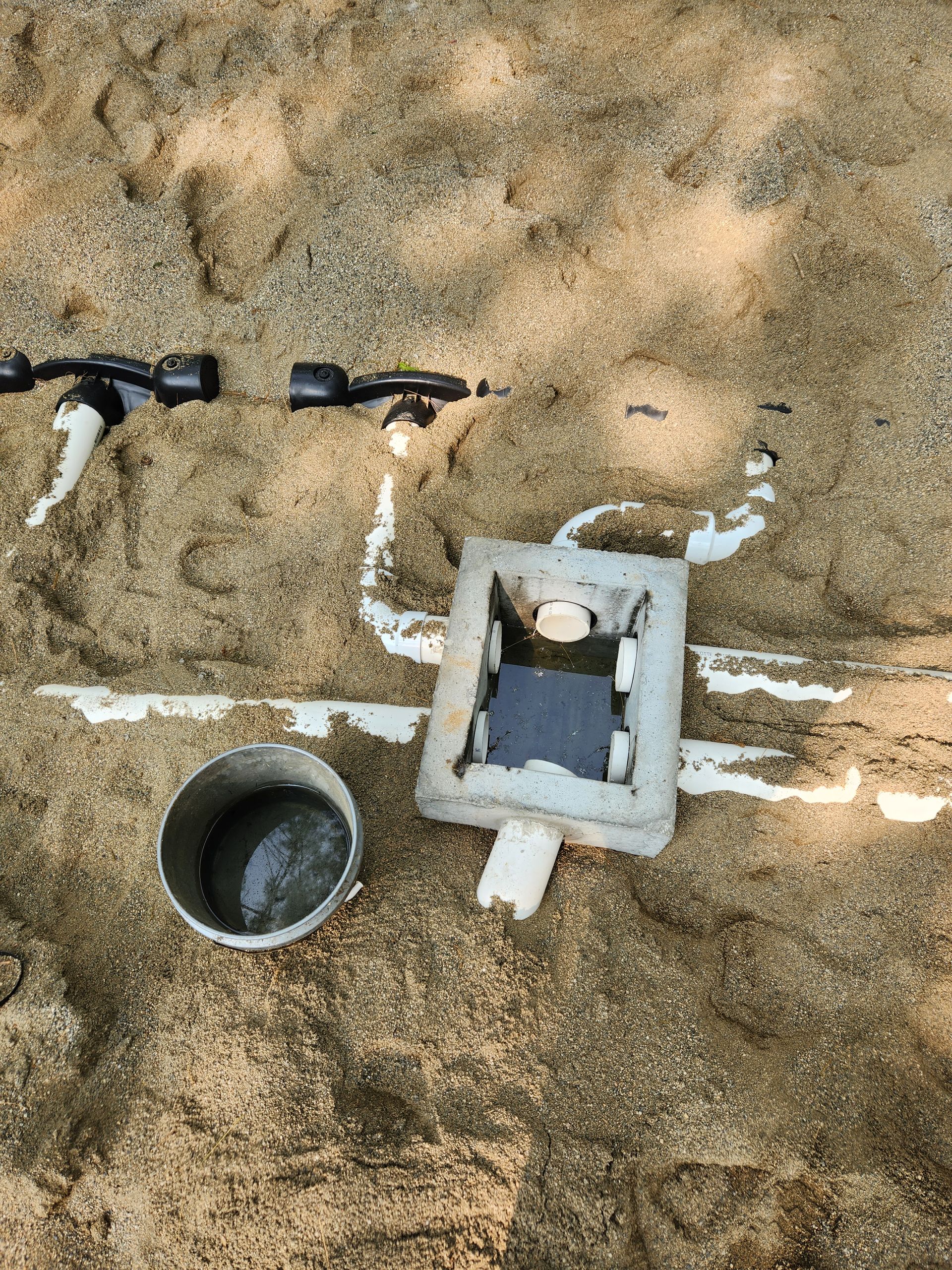 a drain pipe is sitting in the sand next to a bucket