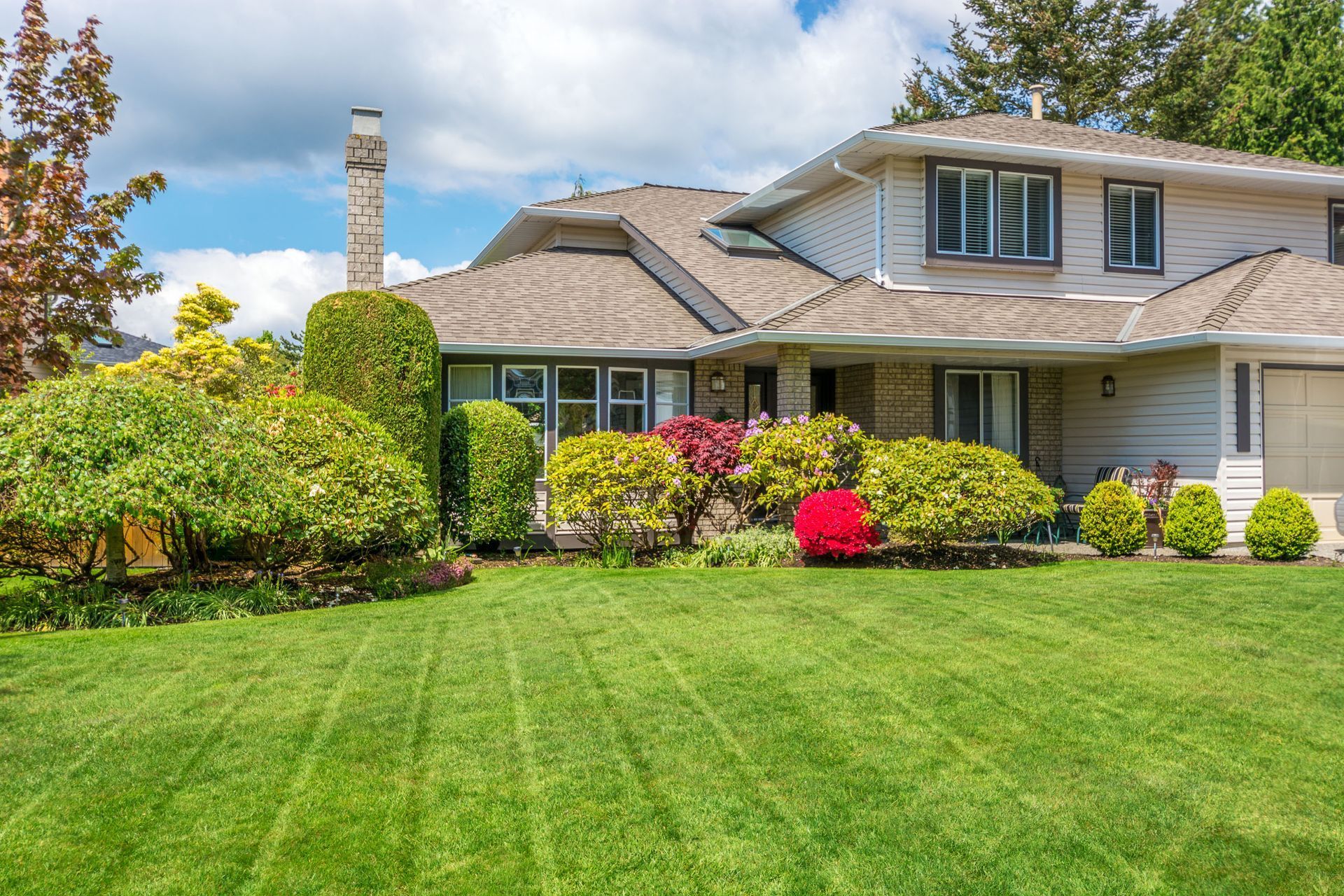 Suburban house with manicured lawn, colorful shrubs, and blue sky
