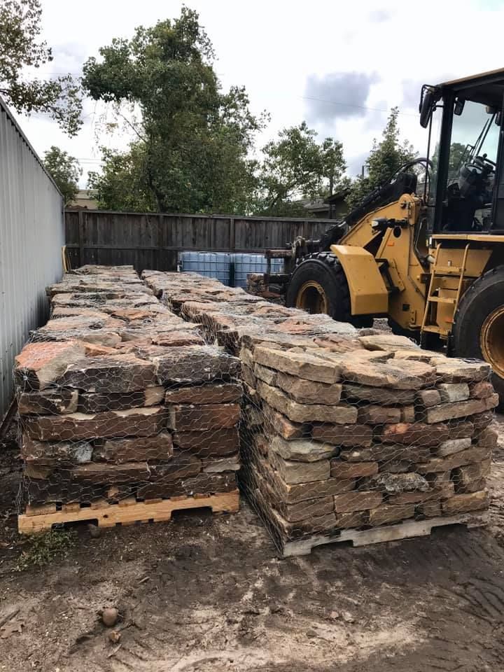 Pallets of stacked stone slabs beside a yellow front loader in an outdoor yard