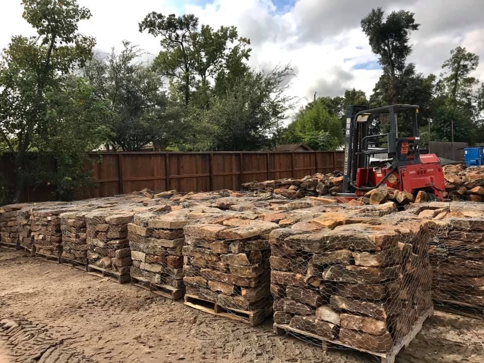 Stacks of stone slabs in a yard, with a forklift and trees in the background.