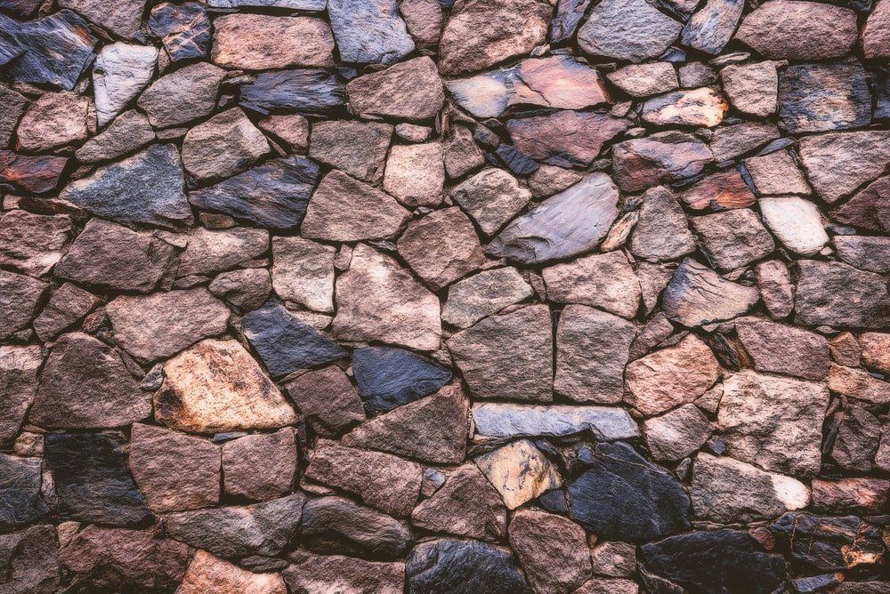 Close-up of a rough stone wall with uneven brown, gray, and pink rocks fused together