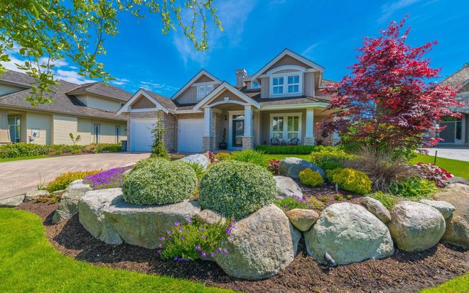 Suburban house with landscaped rock garden, colorful flowers, and a red tree in front yard