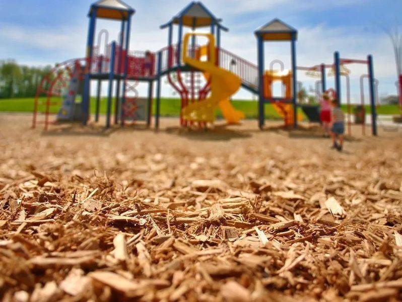Playground with colorful play structures and a yellow slide, seen from a low angle over wood chips.