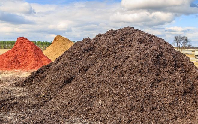 Several piles of mulch in red, yellow, and dark brown outdoors under a cloudy sky