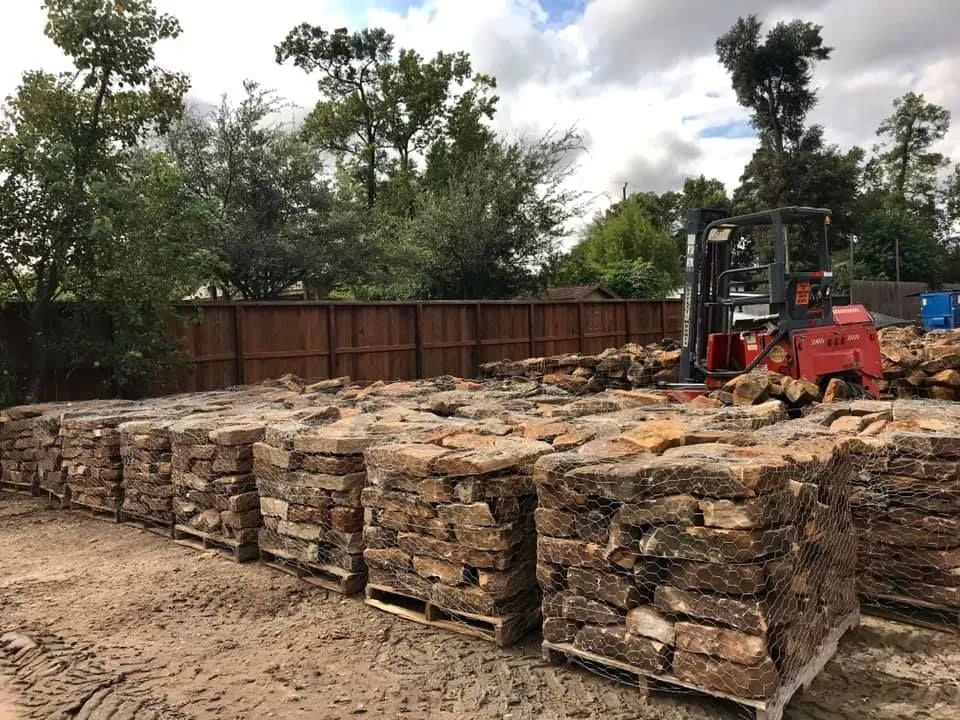 Stacks of cut stone blocks in a yard, with a forklift and trees in the background.