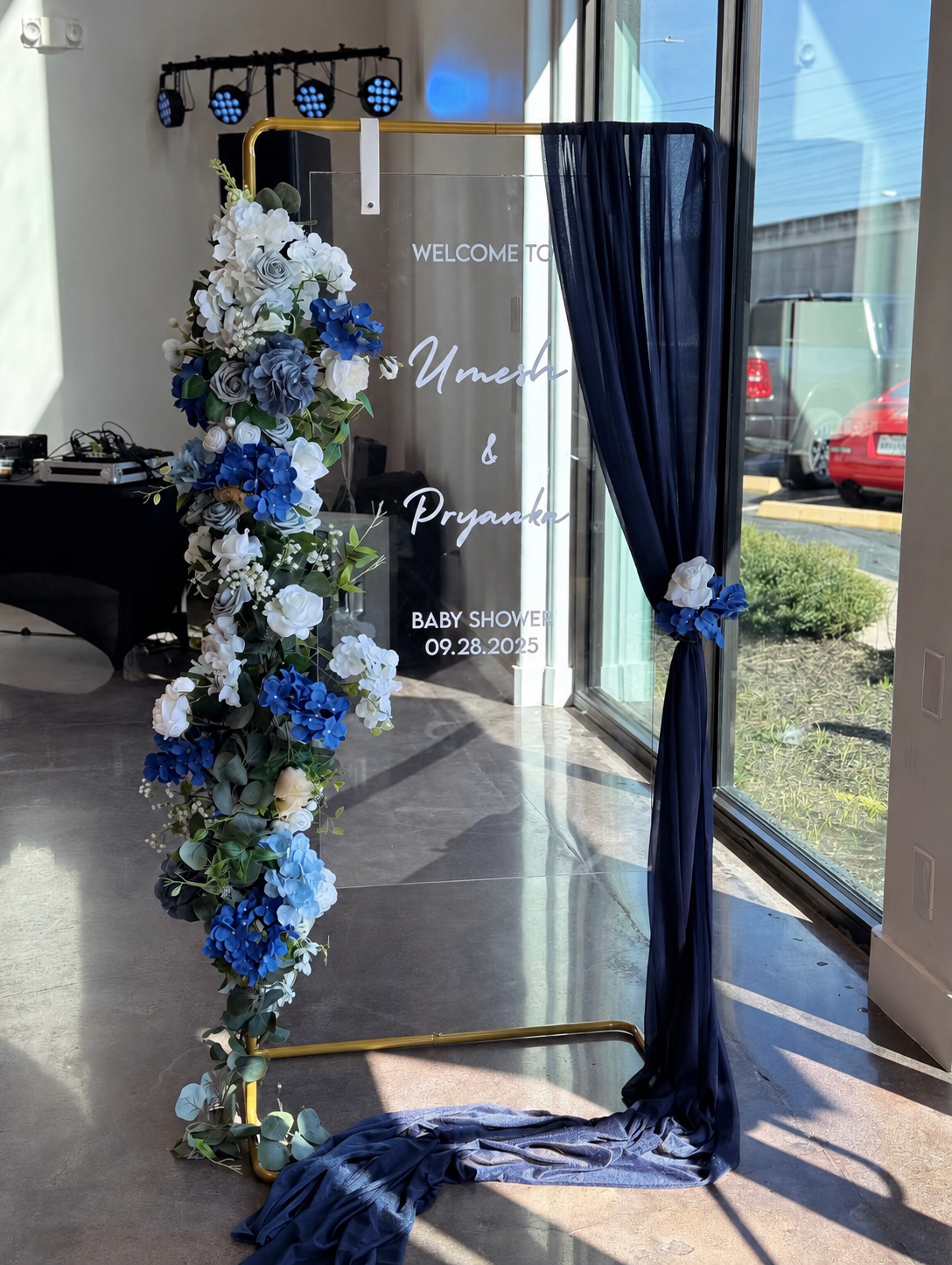 Blue-and-white floral wedding arch with navy curtains beside a glass door at an event venue
