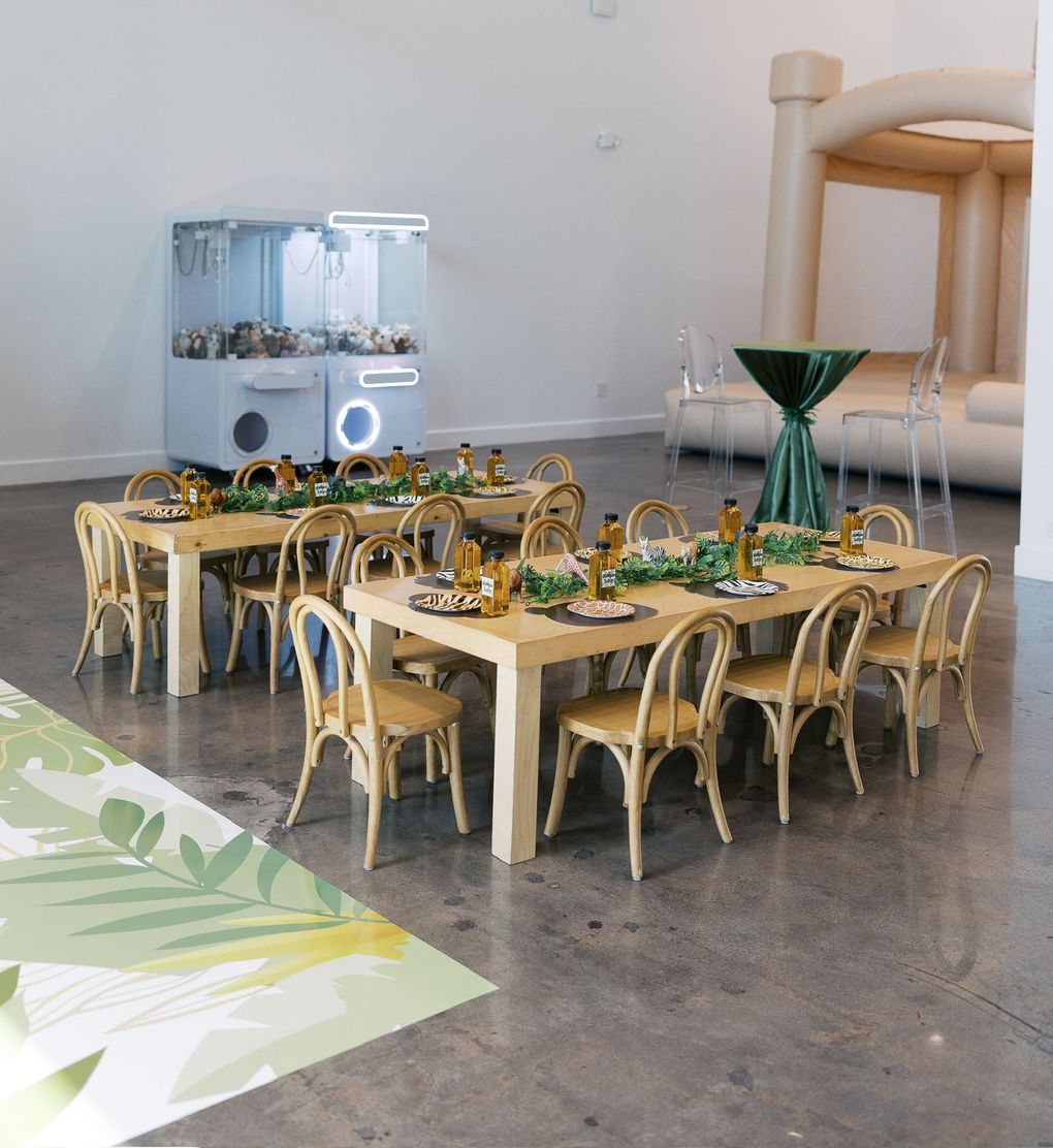 A modern dining setup with two long tables, green glassware, and woven chairs in a bright gallery-like room