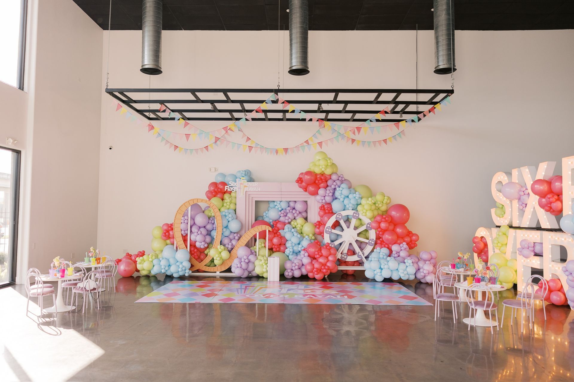 Pastel balloon-decorated party stage with tables and chairs in a bright event hall