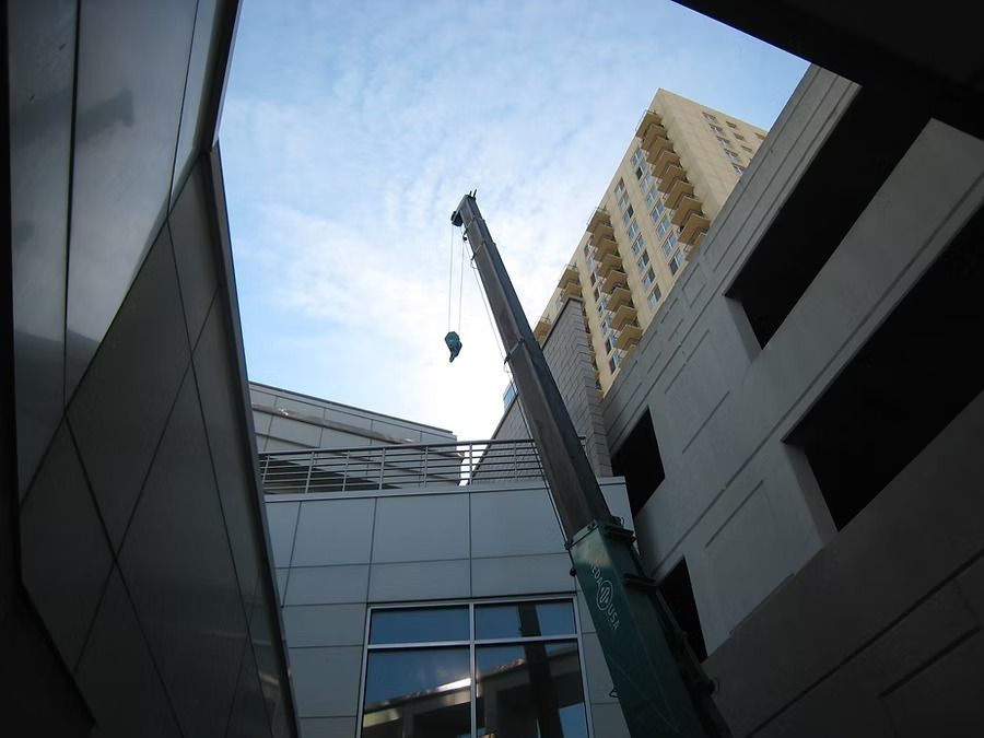 Construction crane reaching toward the sky, between buildings. Blue sky visible.