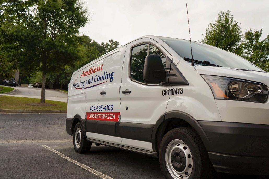 White utility van with company logo parked on a street beside trees and a road sign