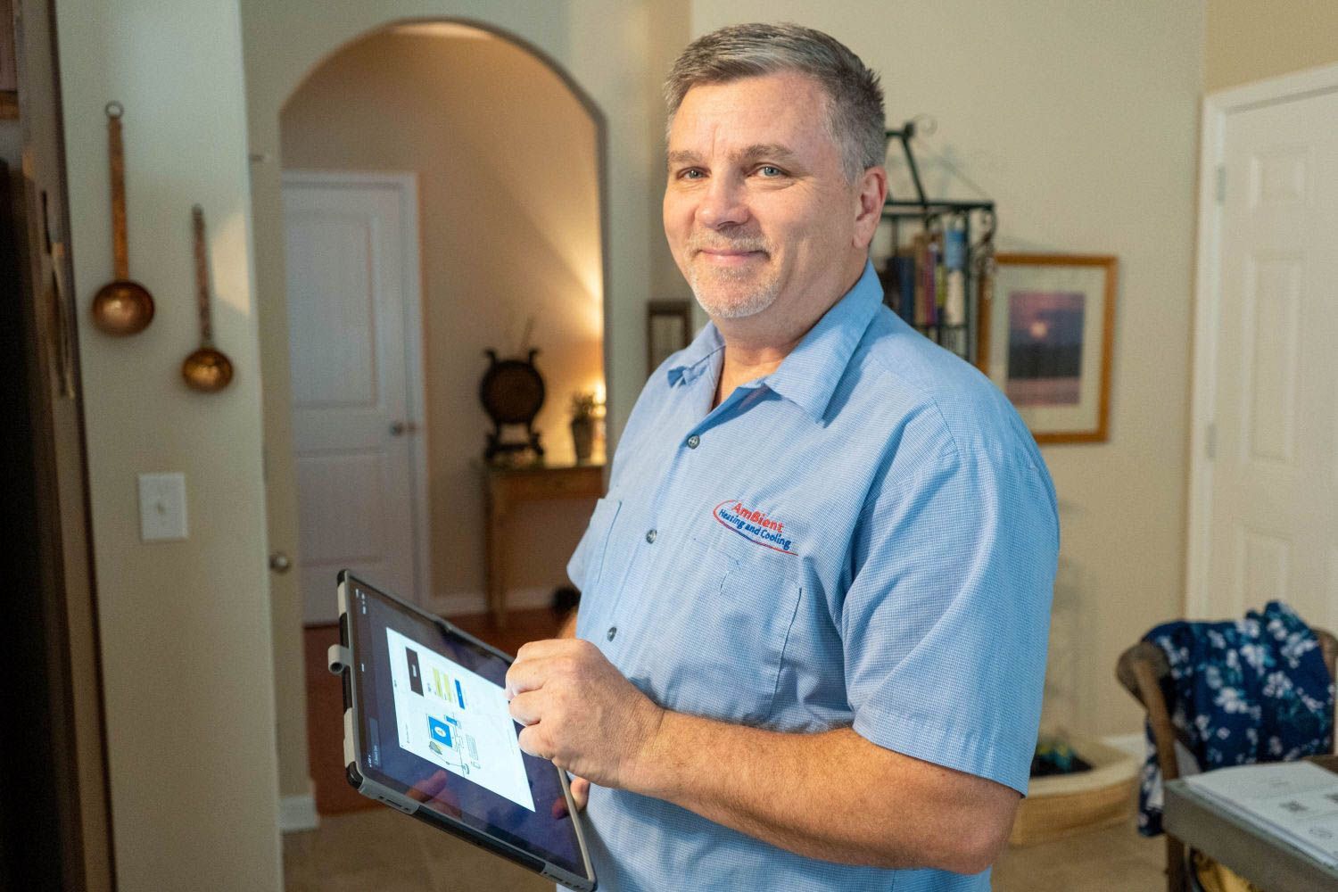 Man holding a tablet in a home interior, standing near an arched doorway and smiling at the camera