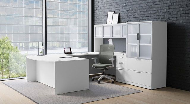 White office desk with gray chair, window, and cabinet with frosted glass doors.