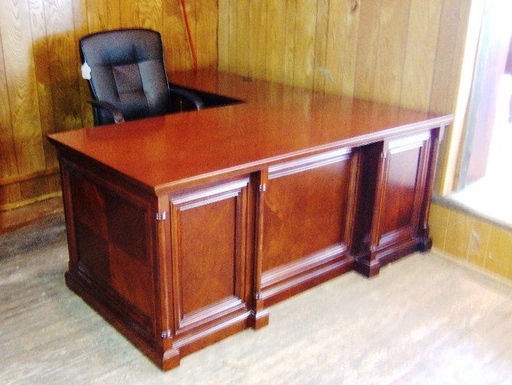 Brown wooden L-shaped desk with a black office chair in a room with wood paneling.