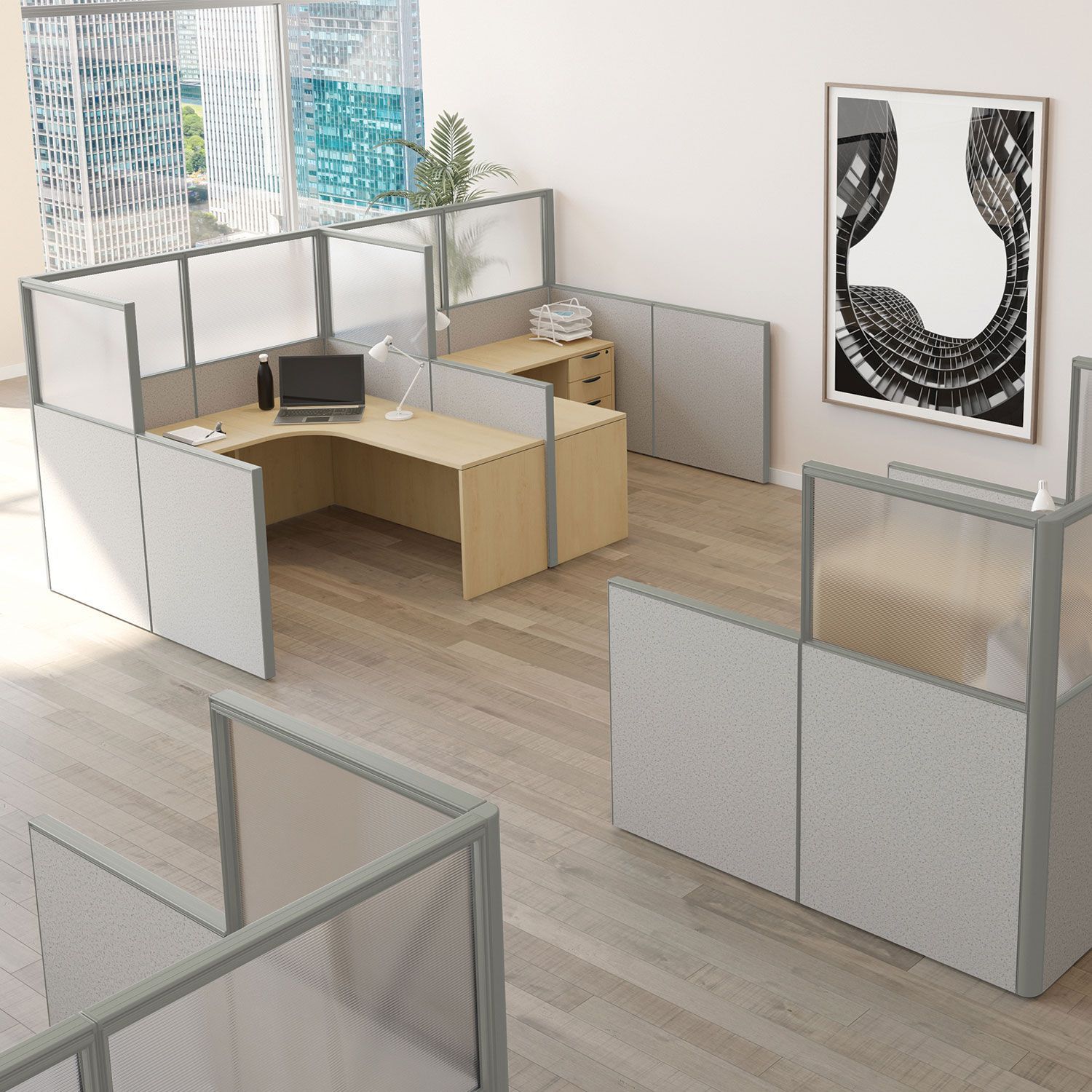 Office cubicles with light wood desks, gray panels, and large windows.