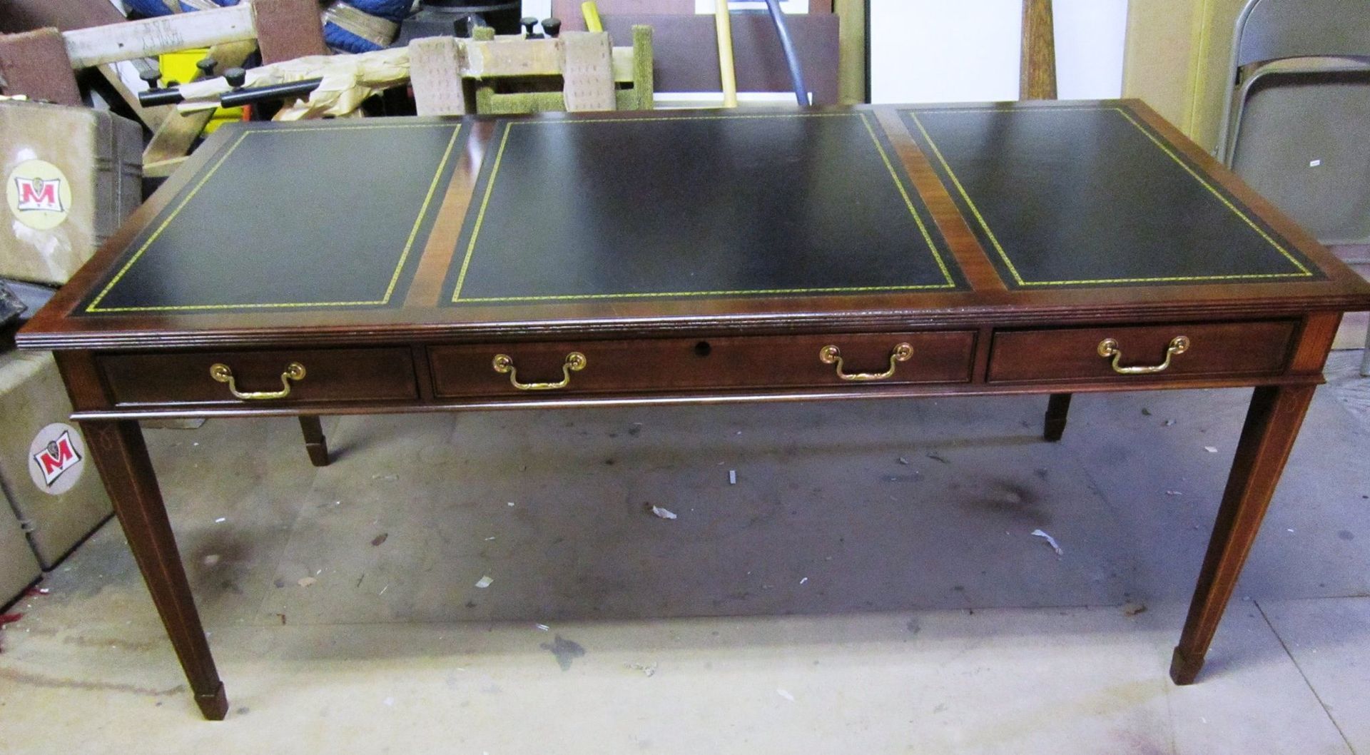 Wooden desk with three black leather panels, brass drawer pulls, and four legs.