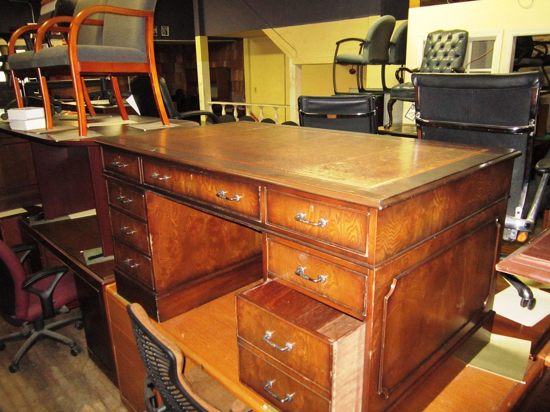 Wooden desk with drawers, sitting on top of other office furniture in a cluttered room.