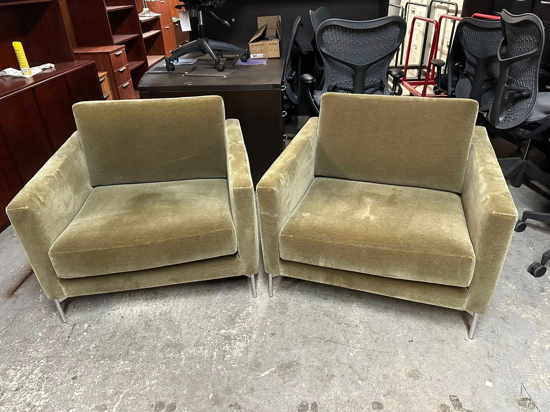 Two olive green upholstered armchairs with silver legs.