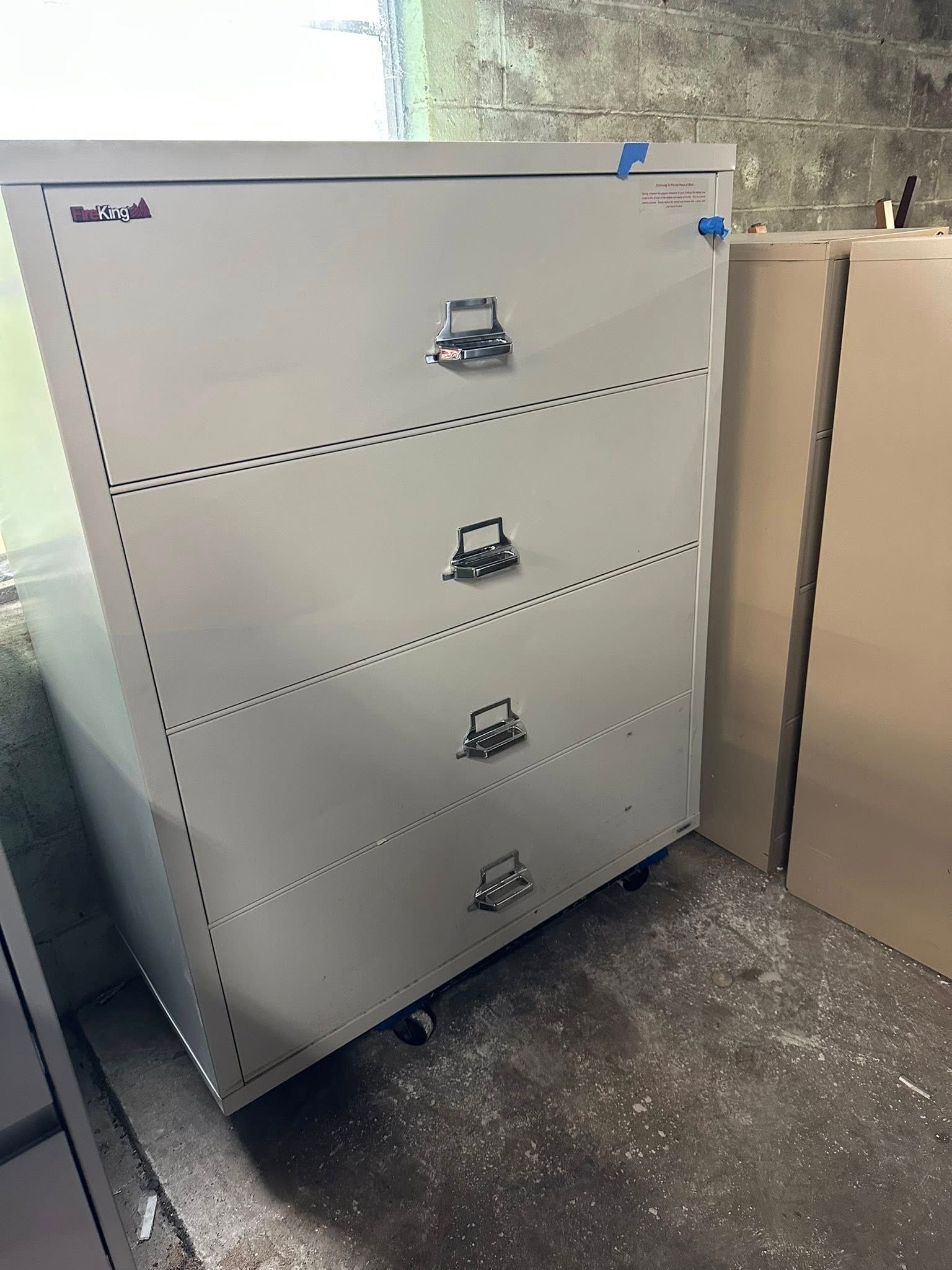 A light gray, four-drawer file cabinet on wheels, in a storage area.